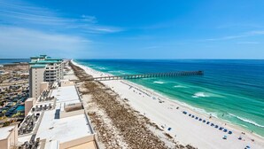 Ein Strandhotel mit einer Pier, die sich ins Meer erstreckt, einem Sandstrand und einem Parkplatz.