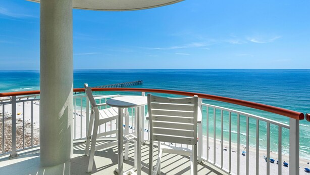 Ein Balkon mit Blick auf den Ozean und den Strand, weiße Möbel und einem Geländer.
