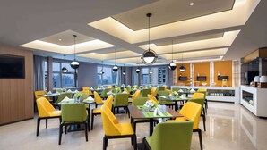 Un espace repas moderne avec des chaises jaunes et vertes, des tables dressées et un coin cuisine en arrière-plan.