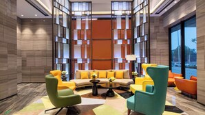 Un hall d’entrée moderne avec un canapé modulable, des fauteuils colorés, une table basse et une cloison décorative en verre.