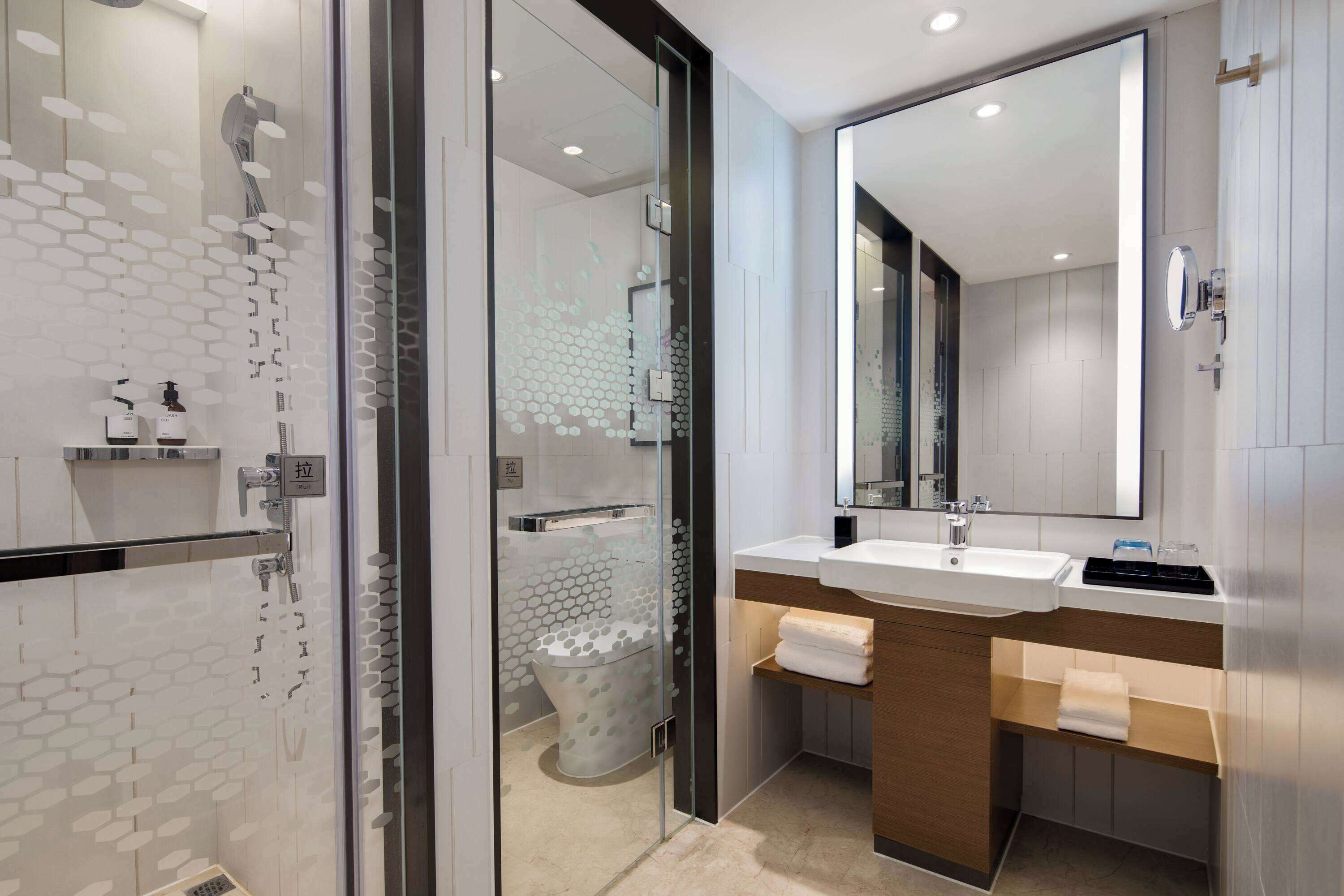 A modern bathroom with a glass-enclosed shower, a large mirror, and a wooden vanity with a sink.