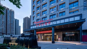 Ein moderner Hotelzugang mit einer großen Schild für "RAMADA by WHIAM" und einer Statue einer Figur davor.