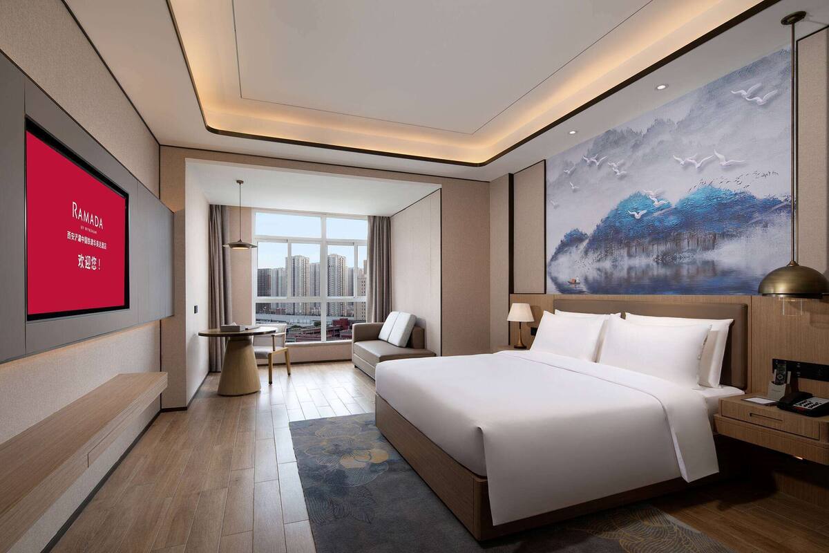 Een moderne hotelkamer met een groot bed, een bureau, een sofa en uitzicht op de stad.