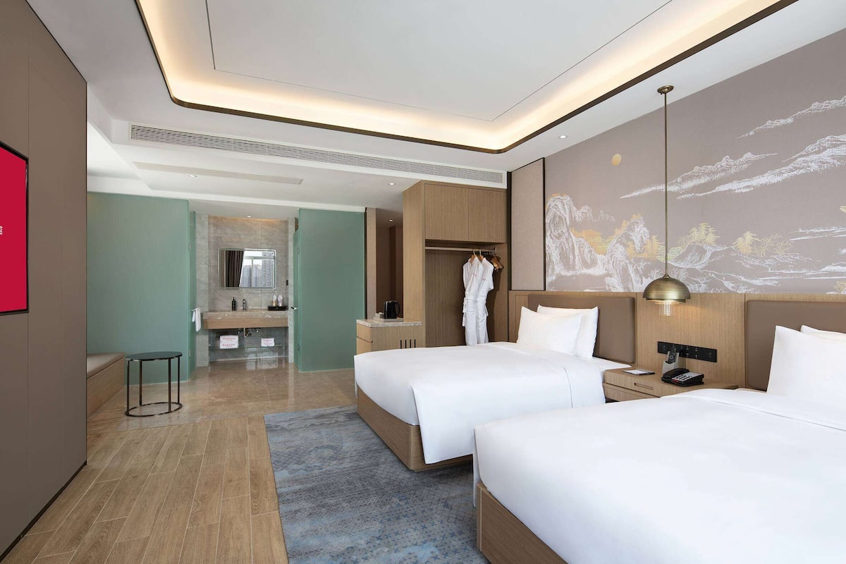 Een hotelkamer met twee bedden, een kledingkast, een kaptafel met spiegel en een kunstwerk aan de muur.