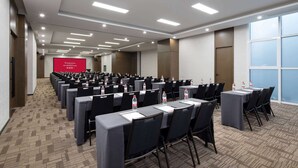Ein Konferenzraum mit Tischen und Stühlen, ausgestattet mit Wasserflaschen und Namensschildern, und einer roten Leinwand mit der Aufschrift 'Ramada' und 'Willkommen im Ramada'.