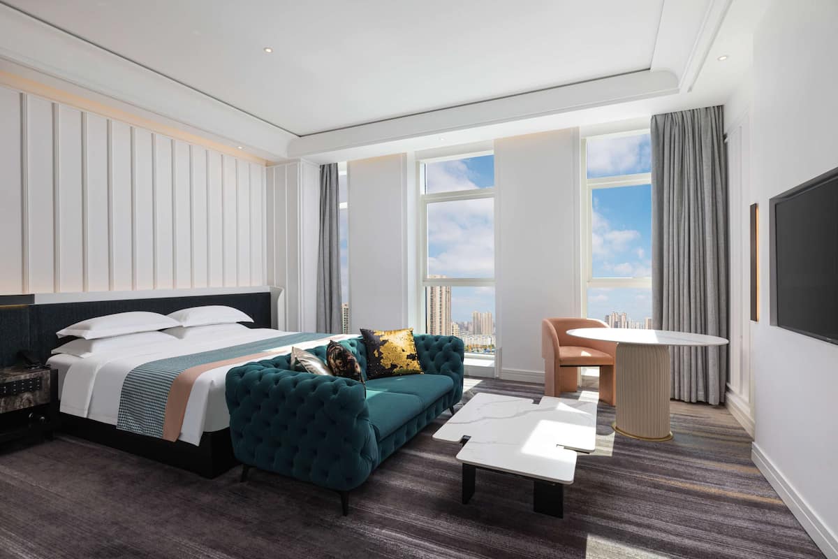 Une chambre d’hôtel moderne avec un grand lit, un canapé, une table à manger et une vue sur la ville.