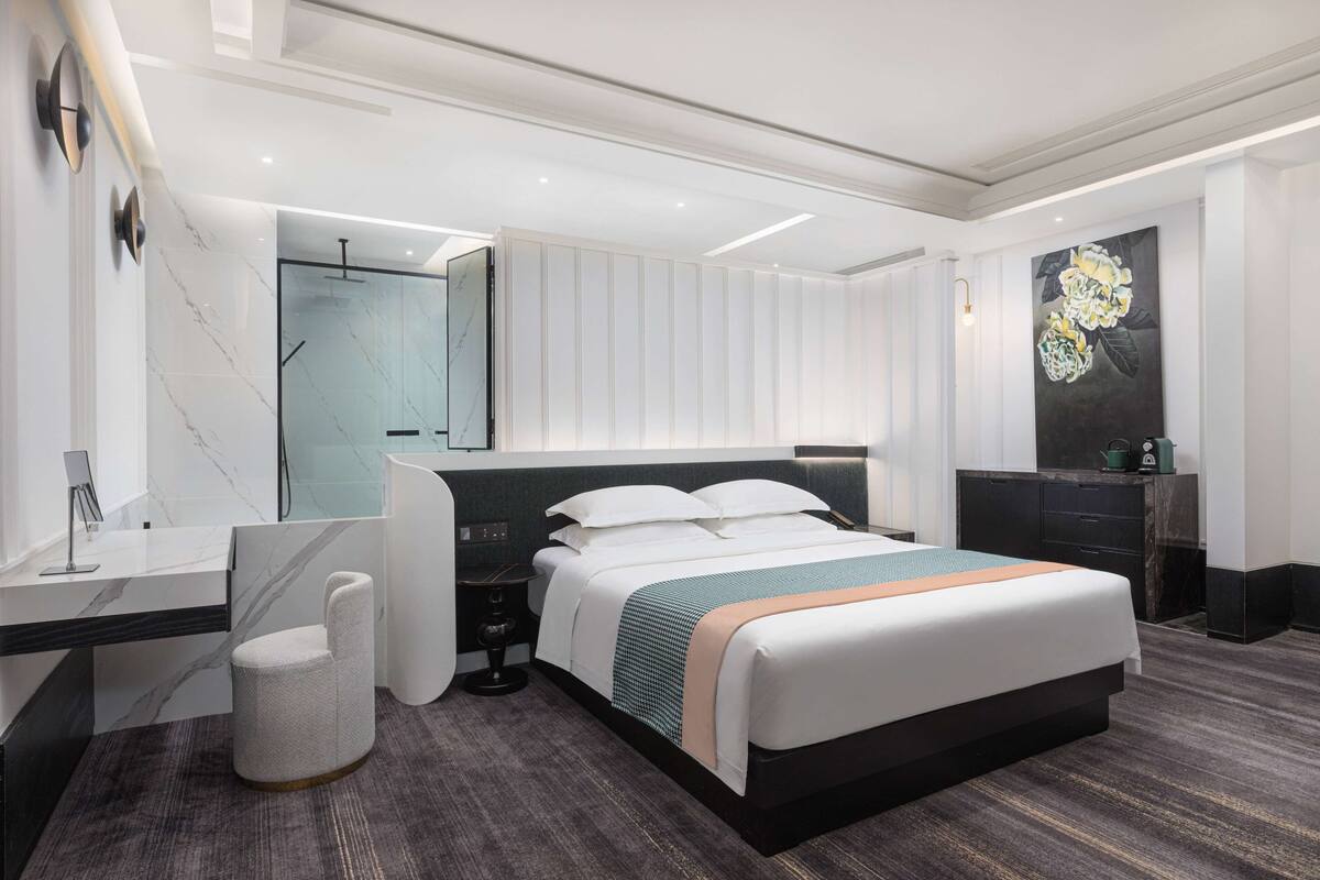 Une chambre d’hôtel moderne équipée d’un grand lit, d’un bureau, d’une chaise, d’une coiffeuse et d’un espace douche.