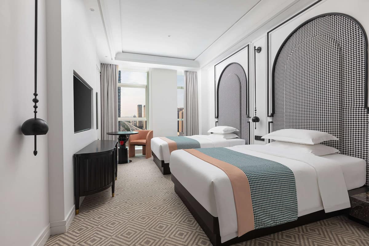 Une chambre d’hôtel avec deux lits, un bureau, une chaise et une grande fenêtre donnant sur la ville.
