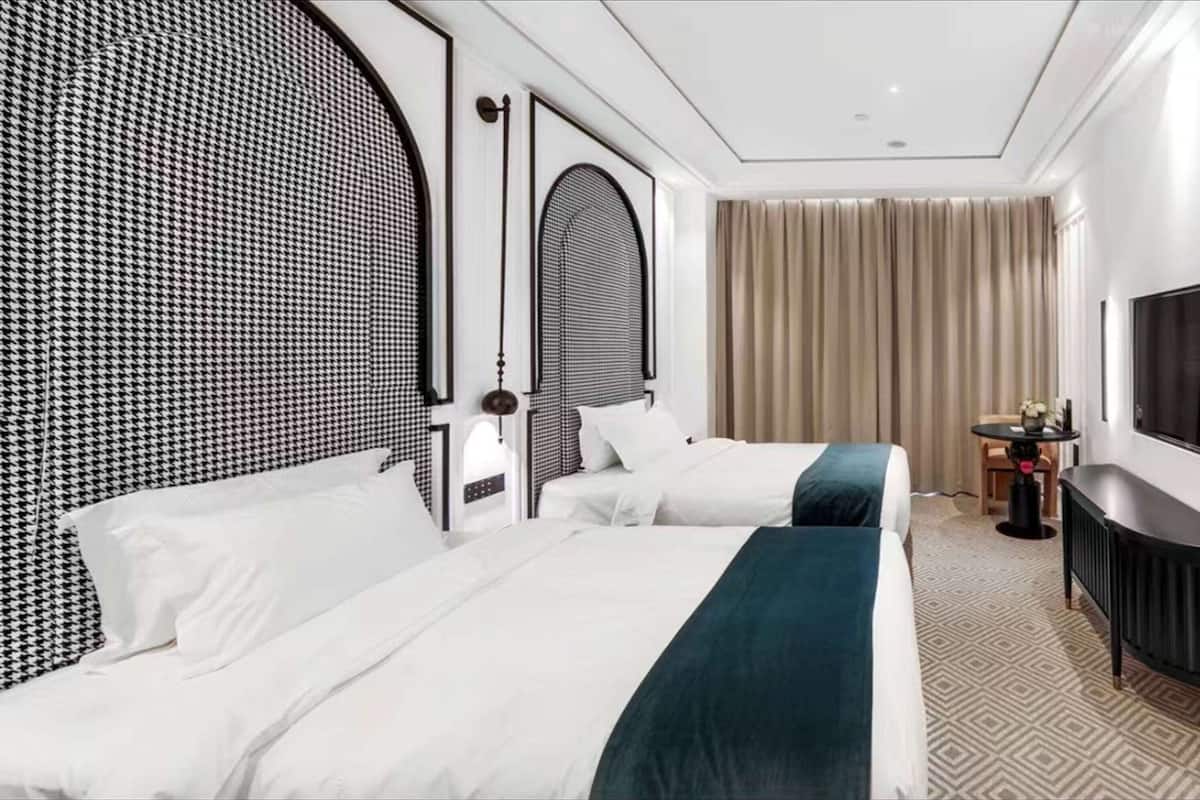 Une chambre d’hôtel avec deux lits, un grand miroir, une télévision et une petite table sur laquelle se trouve un vase.