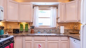 A kitchen with light-colored cabinets, a gas stove, a sink, and a window with curtains.