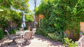 A patio with a table and chairs, surrounded by lush greenery and a wooden fence.