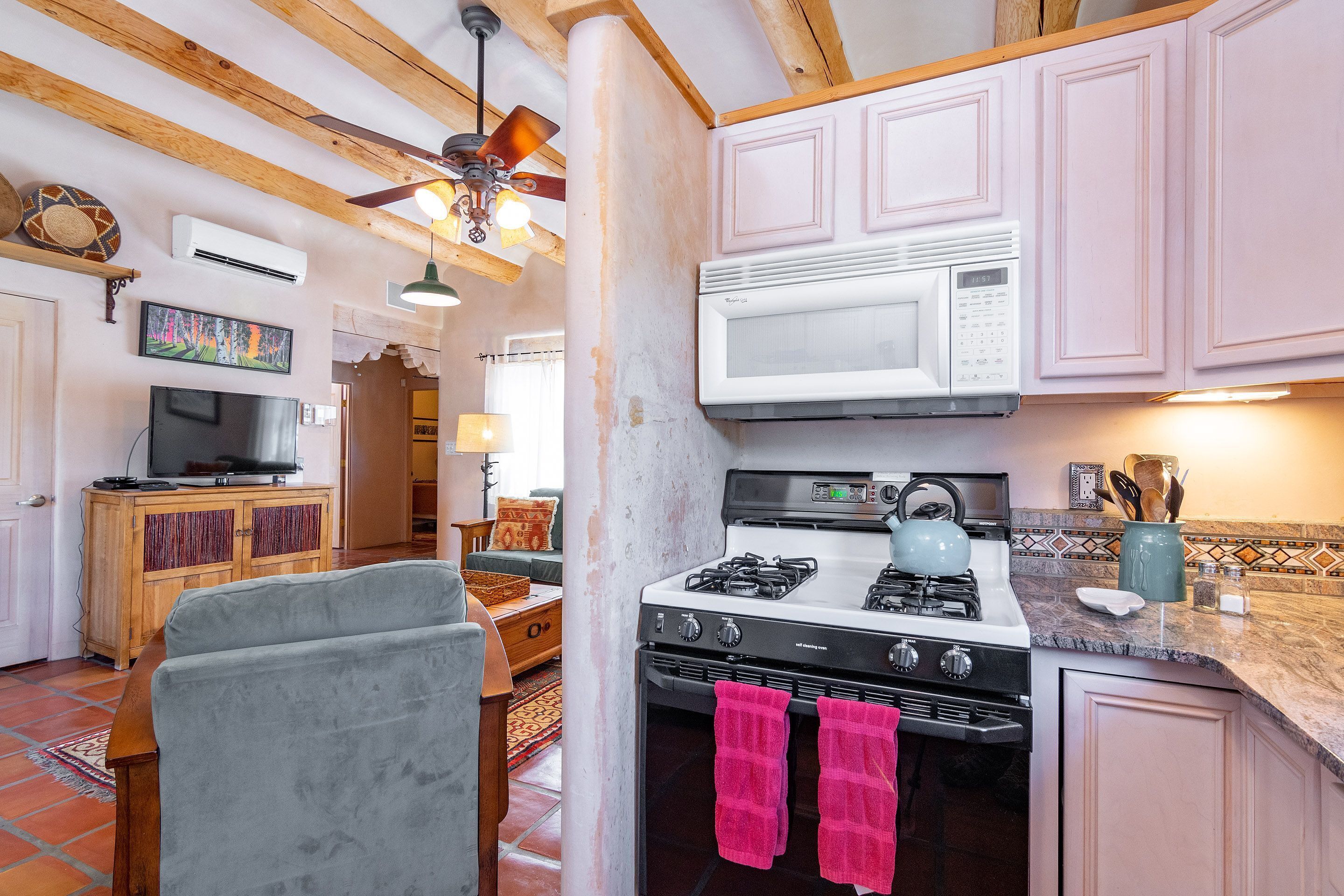A kitchen with a gas stove, a microwave, and pink towels hanging on the oven door.