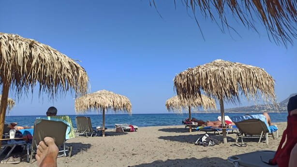 A beach with thatched umbrellas and lounge chairs, a clear blue sky, and the sea in the background. - Traditional Cretan stone cottage on the semi-rural outskirts of Kefalas, Vamos (Kefalas)