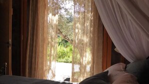 A room with a bed, curtains, and a view of greenery outside. - Traditional Cretan stone cottage on the semi-rural outskirts of Kefalas, Vamos (Kefalas)