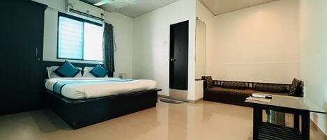 A bedroom with a bed, a bedside table, a sofa, a ceiling fan, and a window.