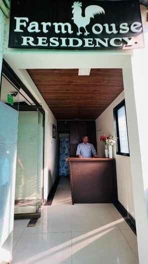 A reception desk with a sign reading 'Farmhouse Residency' and a person standing behind it. - Farmhouse Residency (Vasai)