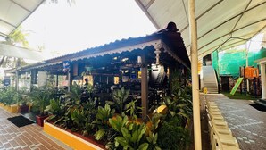A covered outdoor area with a tiled floor, potted plants, and a play area with a slide. - Farmhouse Residency (Vasai)