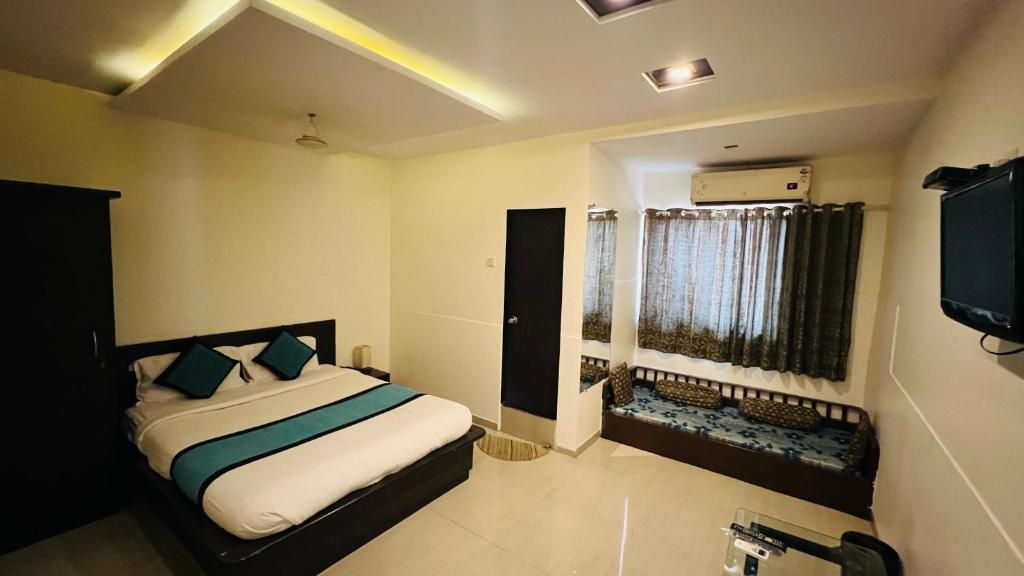 A hotel room with a bed, a television, an air conditioning unit, and a window with curtains.