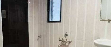 Un baño con inodoro, lavamanos, un cubo rojo y una pantalla pequeña montada en la pared.