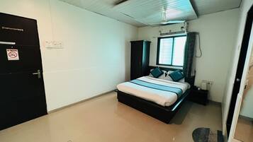 A hotel room with a bed, a wardrobe, a door with a 'No Smoking' sign, and a window with curtains.