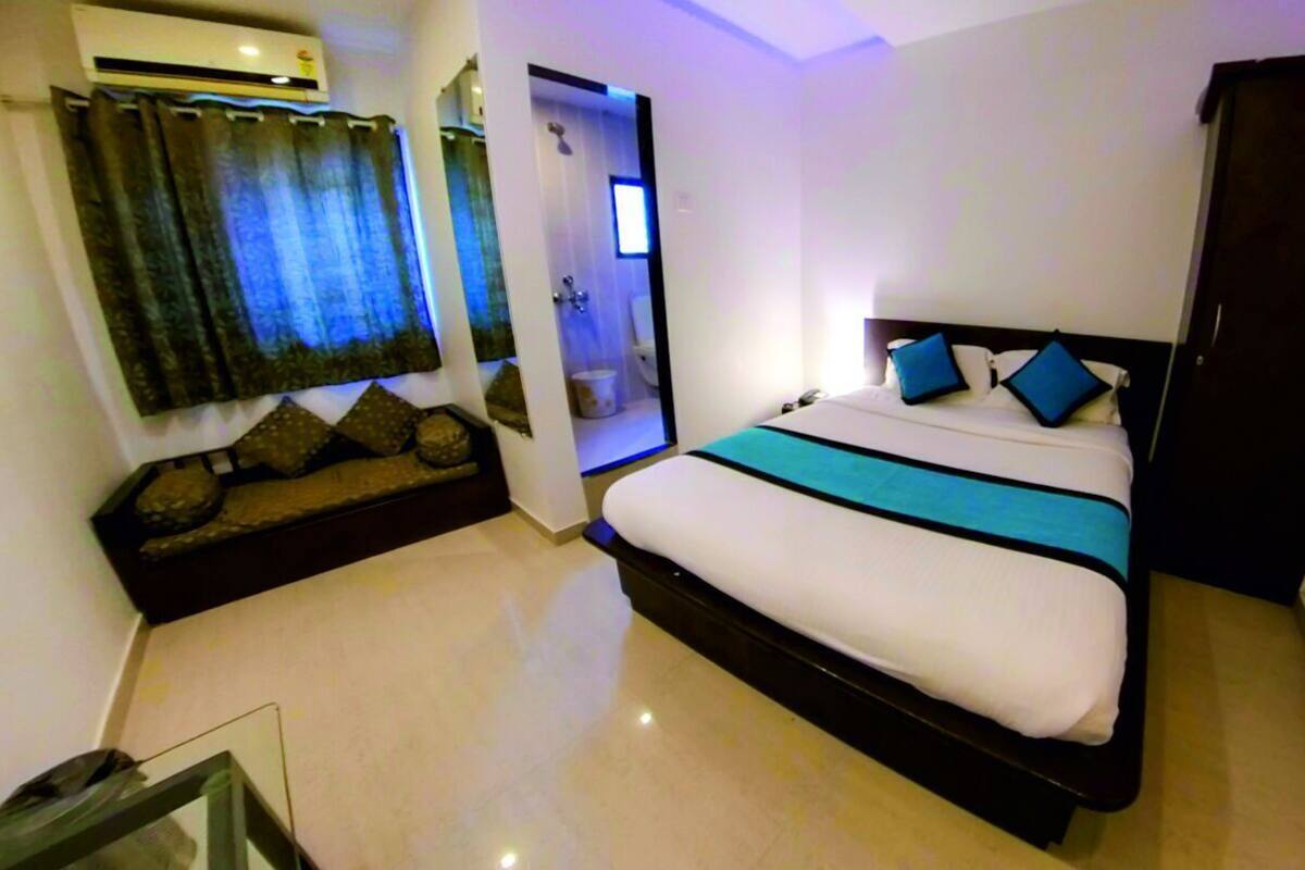 A bedroom with a bed, a sofa, an air conditioning unit, and a bathroom door.