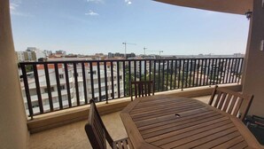 Un balcon avec une table et des chaises en bois, offrant une vue sur le paysage urbain, avec ses bâtiments et ses grues de construction.