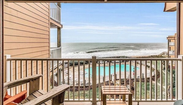 A balcony with a view of the ocean, a pool, and a wooden deck.