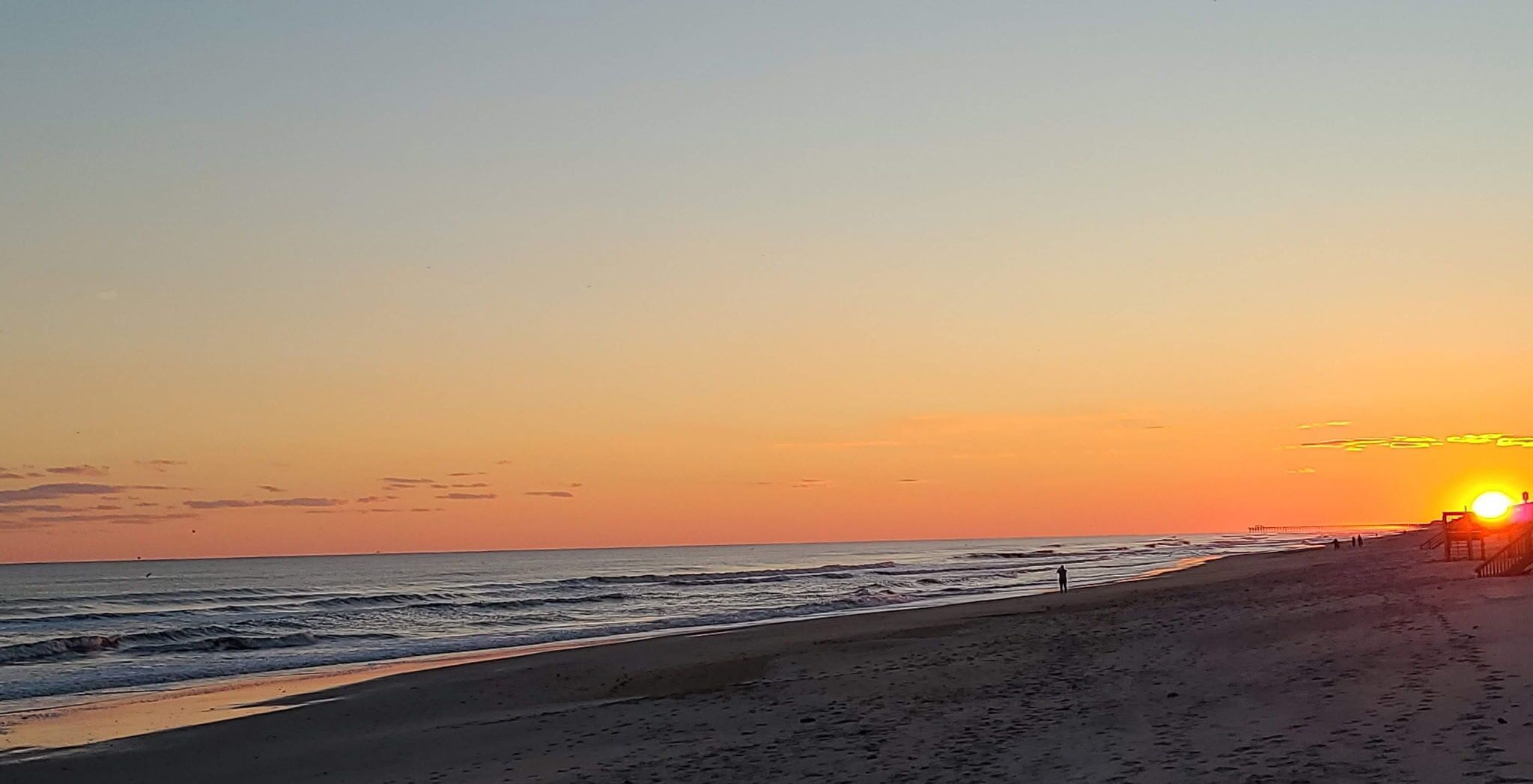 Une plage avec une promenade en bois et un coucher de soleil en arrière-plan.