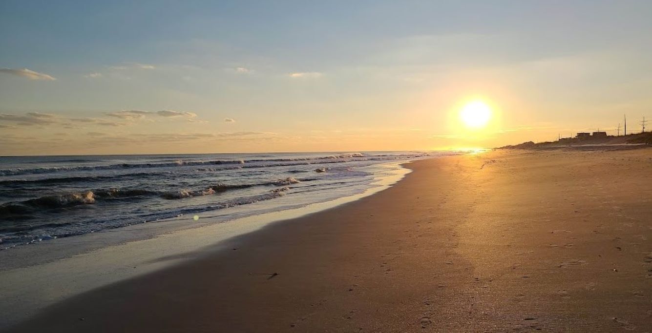 Una playa al atardecer con cielo despejado y olas tranquilas.