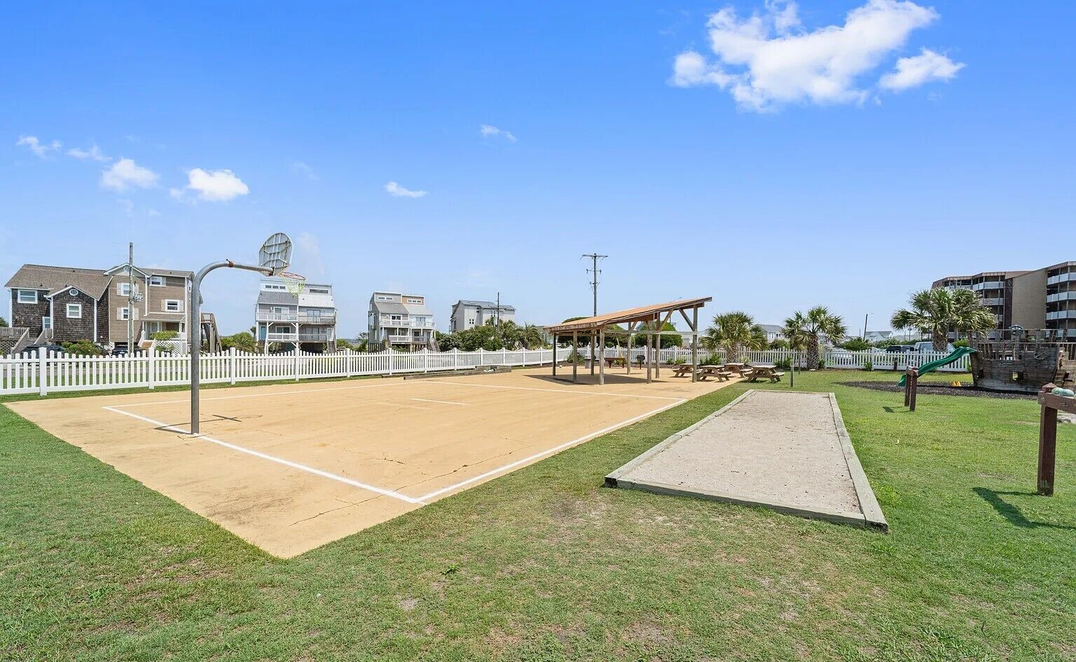 A sports court with a pavilion, surrounded by a white fence and residential buildings.