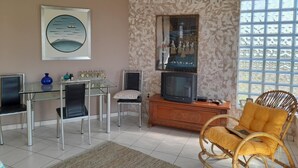 Een woonkamer met een televisie, stoelen, een bank, een decoratieve spiegel en een raam met uitzicht.