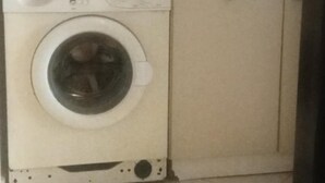 Een praktische wasruimte met een wasmachine, een klein strijkplank en een wasmand.