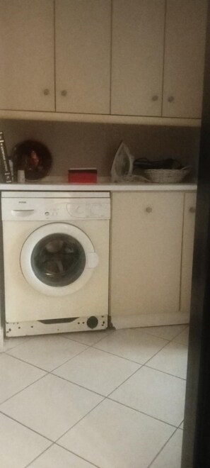 Ein kleiner Waschbereich mit Waschmaschine, Bügelbrett und Wäschekorb.