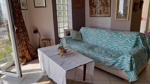 Een kamer met een bank, een tafel met decoratie, een raam met gordijnen, en wanddecoratie.