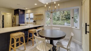 Una cocina moderna con una isla central, taburetes blancos tipo bar, una mesa de comedor redonda y una araña.