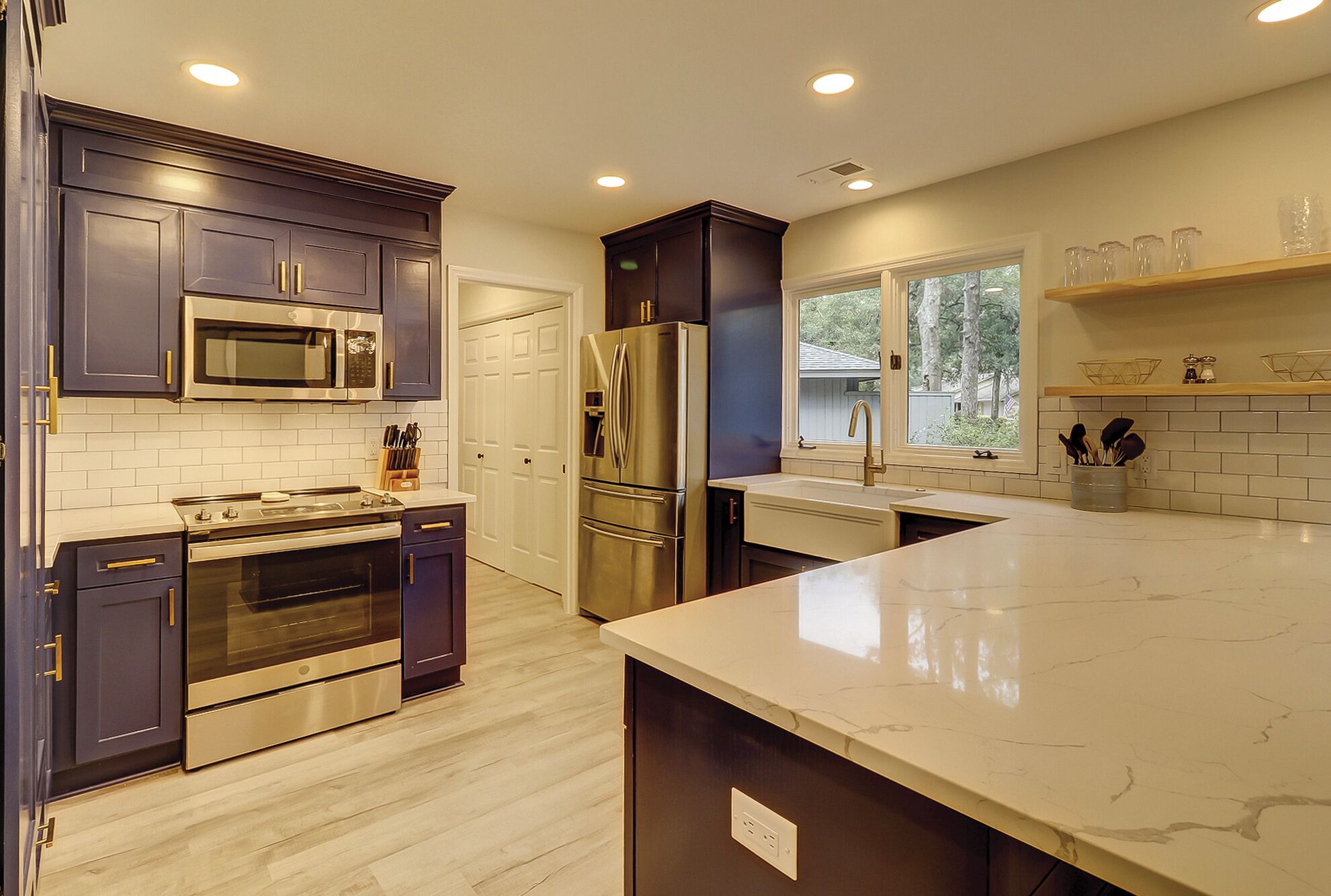 A modern kitchen with dark cabinets, stainless steel appliances, a marble countertop, and a window providing a view of the outdoors.