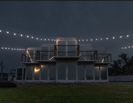 Un edificio moderno de varios niveles y amplios ventanales, rodeado de césped y luces de cadena.