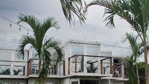 Una casa moderna de concepto abierto con fachada de vidrio, rodeada de palmeras y un césped.