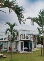 Una casa moderna de concepto abierto con fachada de vidrio, rodeada de palmeras y un césped.