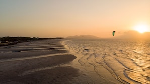 Una playa con barcos y una persona practicando kitesurf.