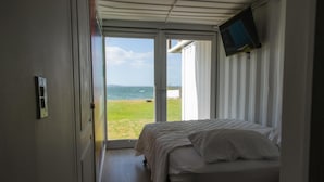 Un dormitorio con cama, televisor montado en la pared y puerta que da a un balcón con vista al mar.