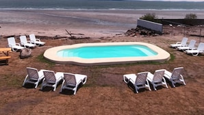 Una piscina rodeada de sillones de descanso, con vista a la playa y al océano al fondo.