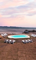 Una piscina rodeada de sillones de descanso, con vista a la playa y al océano al fondo.