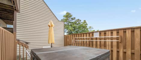 A hot tub in a backyard with a wooden fence and a covered patio area.