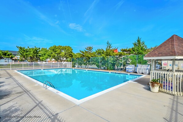 A rectangular swimming pool with a white border, surrounded by a fence and potted plants. - Club Ocean Villas II by Coolvacay (Ocean City)