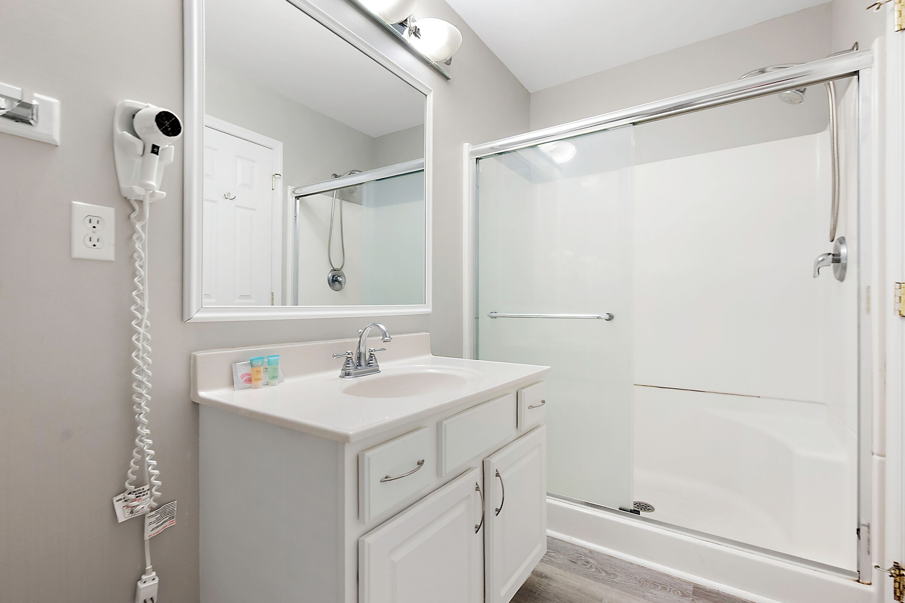 A modern bathroom with a white vanity, a large mirror, a hairdryer, and a glass shower enclosure.