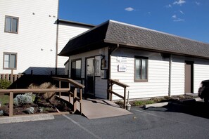 Situated next to a larger building, this single-story villa offers a front entrance with a ramp and a small porch area.