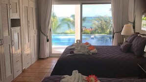 Quarto de hotel com duas camas, ventoinha no teto, vista para o oceano e piscina.