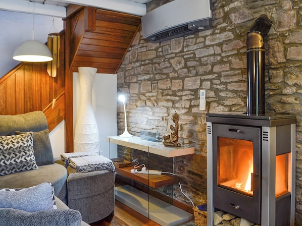 A cozy living room with a stone wall, a sofa, a table with a Buddha statue, and a wood-burning stove.