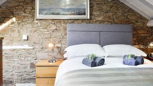 A bedroom with a stone wall, a bed with white linens, two rolled towels, a bedside lamp, and a framed painting. - 1 bedroom accommodation in Merthyr Cynog, near Brecon (Merthyr Cynog, near Brecon)